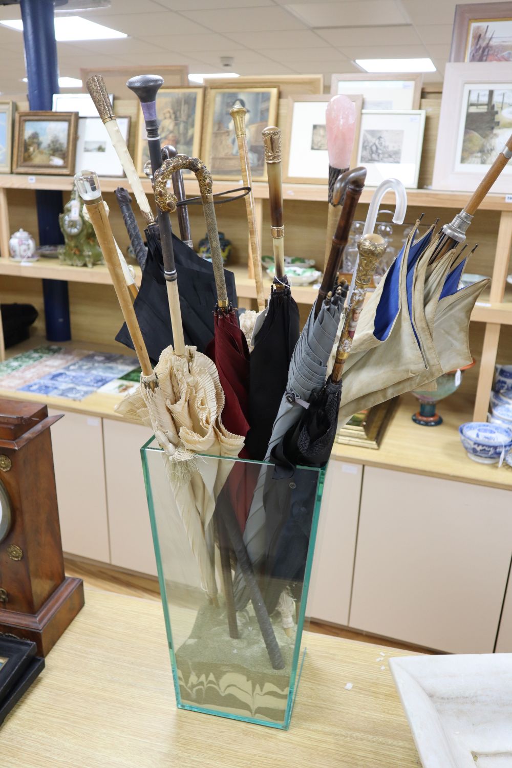 Thirteen various parasols, each with decorative handle, and two walking sticks, contained within a plate glass umbrella stand
